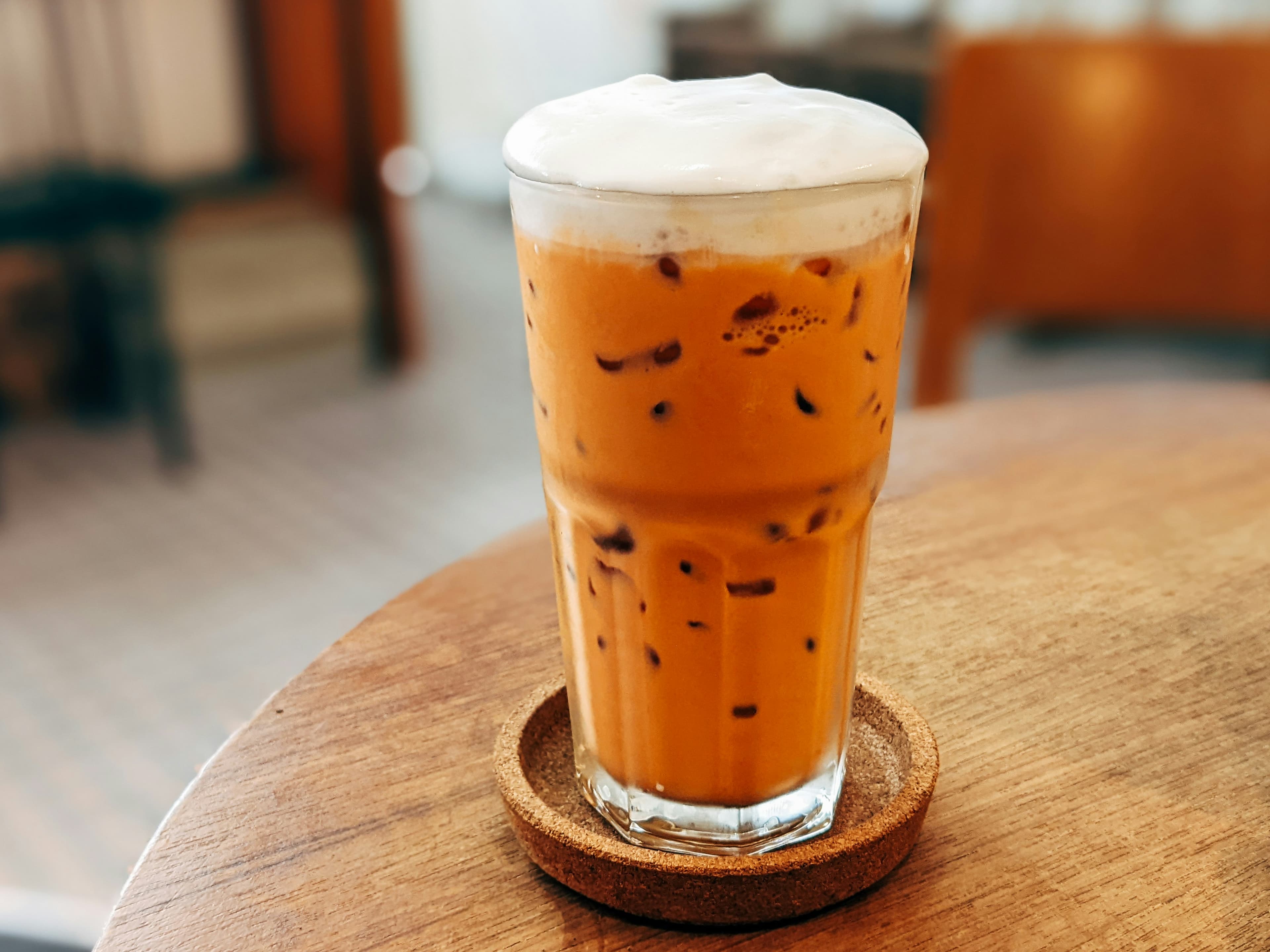 Iced Thai milk tea with milk foam on a cork coaster
